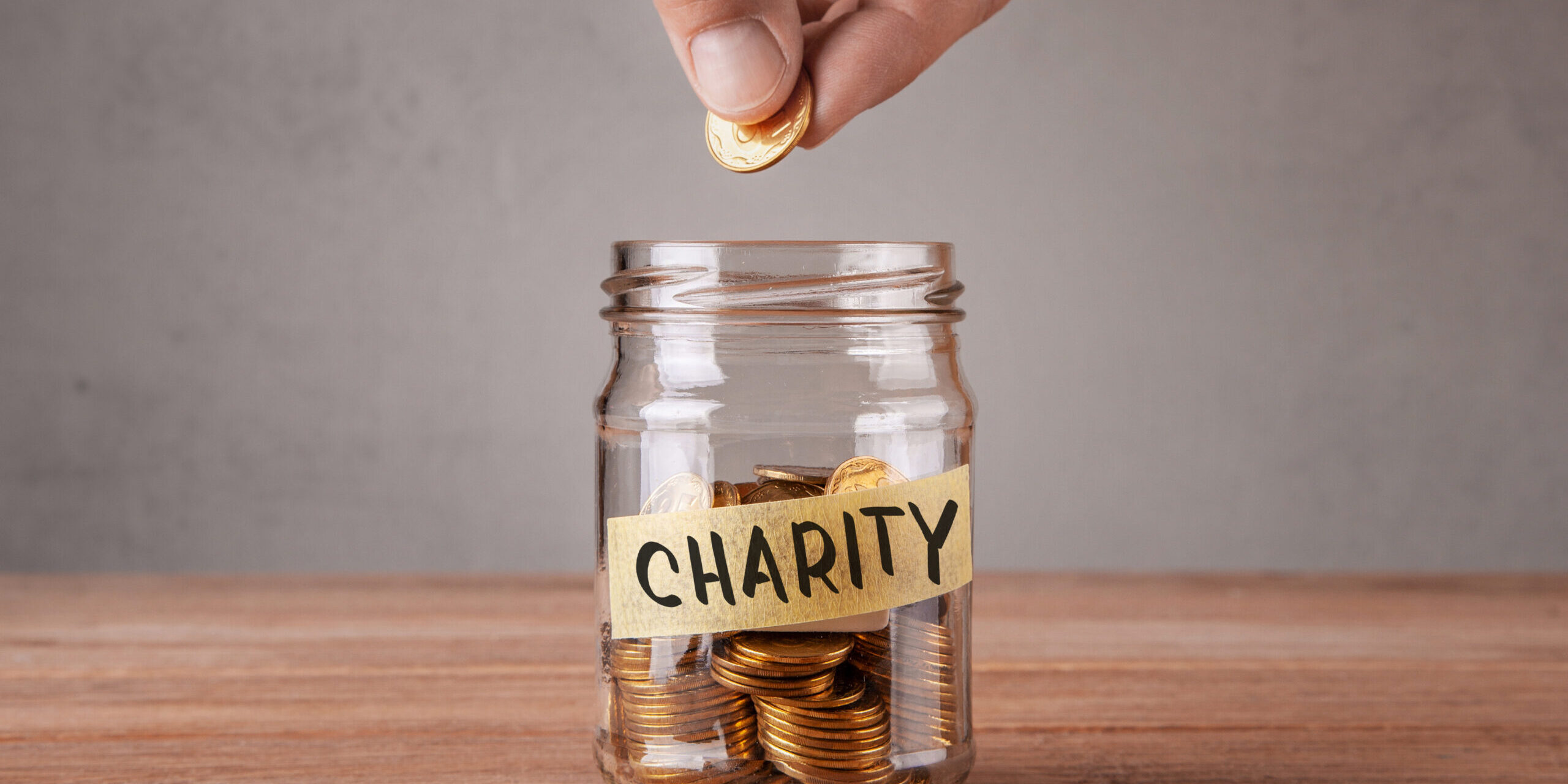 Charity. Glass jar with coins and an inscription charity. Man holds  coin in his hand